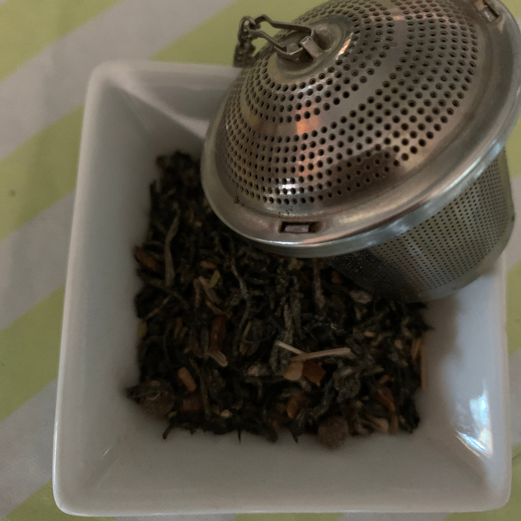 Tea strainer with tea leaves in a white square bowl on a striped background