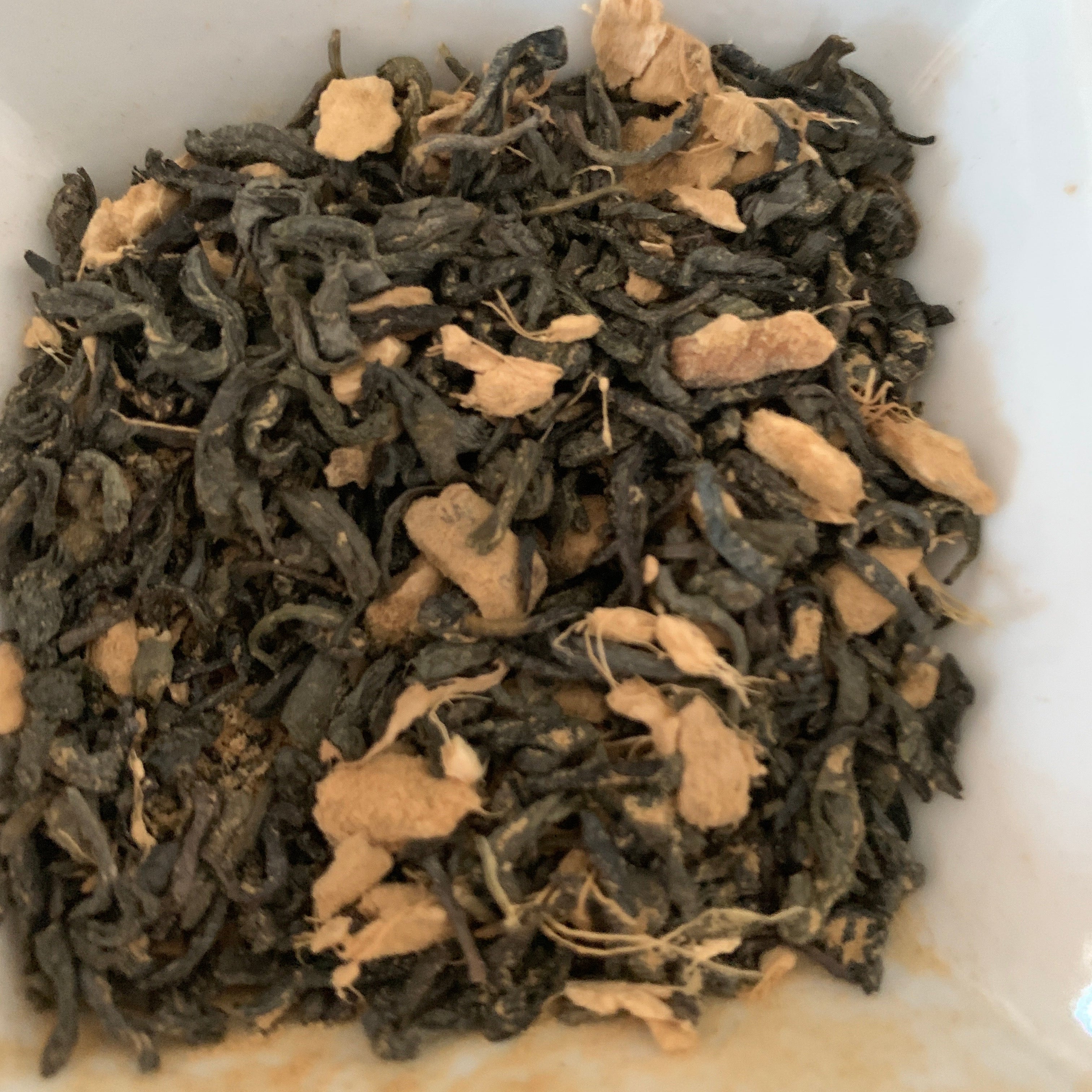 Dry tea leaves with pieces of ginger in a white container
